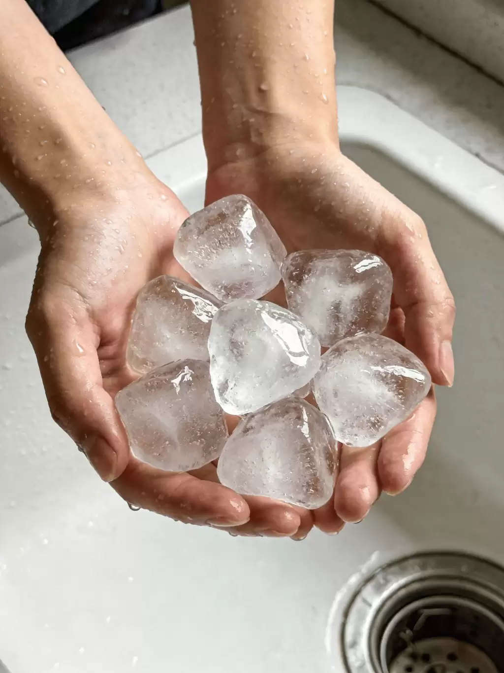jimeng-2026-03-09-4777-双手捧着7颗又大又透的不规则形状的冰块,背景白色厨房水槽,手被冰水打湿.png