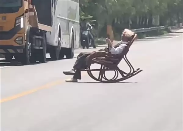 大爷马路中间手拿折扇躺摇椅上晒太阳 过往车辆纷纷减速避让