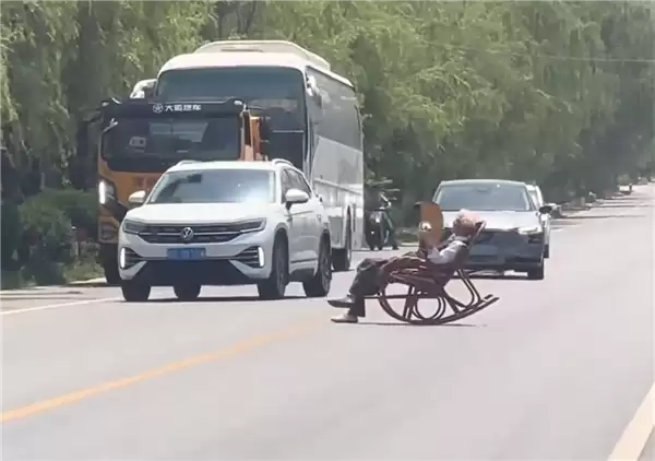 大爷马路中间手拿折扇躺摇椅上晒太阳 过往车辆纷纷减速避让