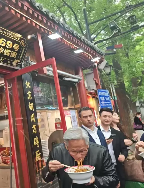 AI教*父黄仁勋穿皮衣现身南锣鼓巷：狂炫老北京炸酱面 喝豆汁露出痛苦面具